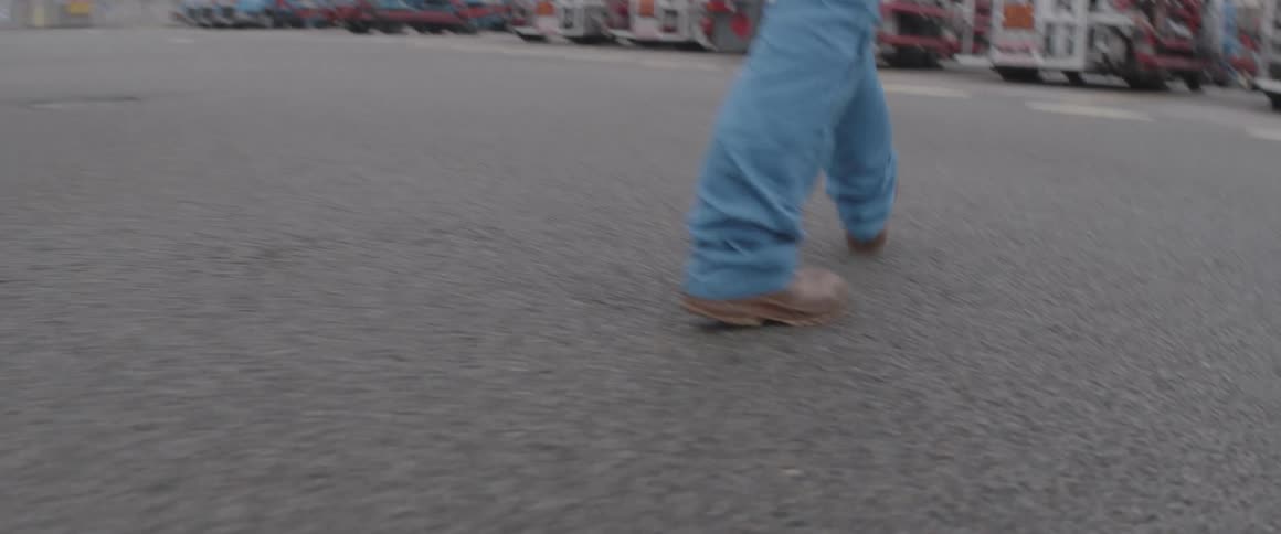 Closeup on the legs of a man walking in a parking lot with fuel vehicles
