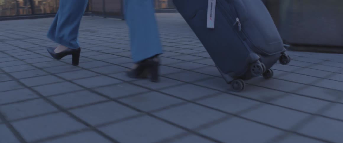 A woman pulls a piece of luggage over a tile floor