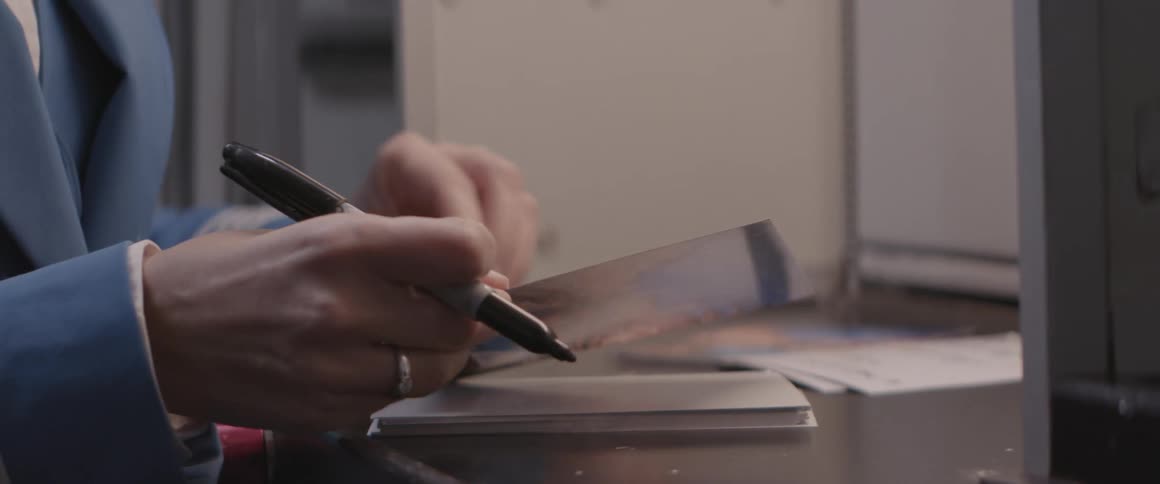 Closeup of a persons hands with a pen writing on a card