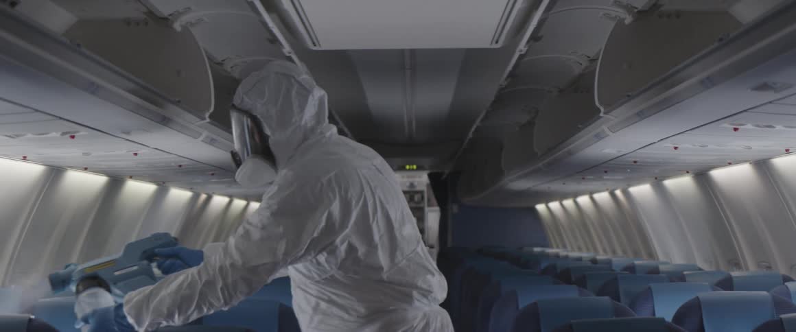 Person wearing protective gear sprays solution onto interior of airplane with a portable sprayer