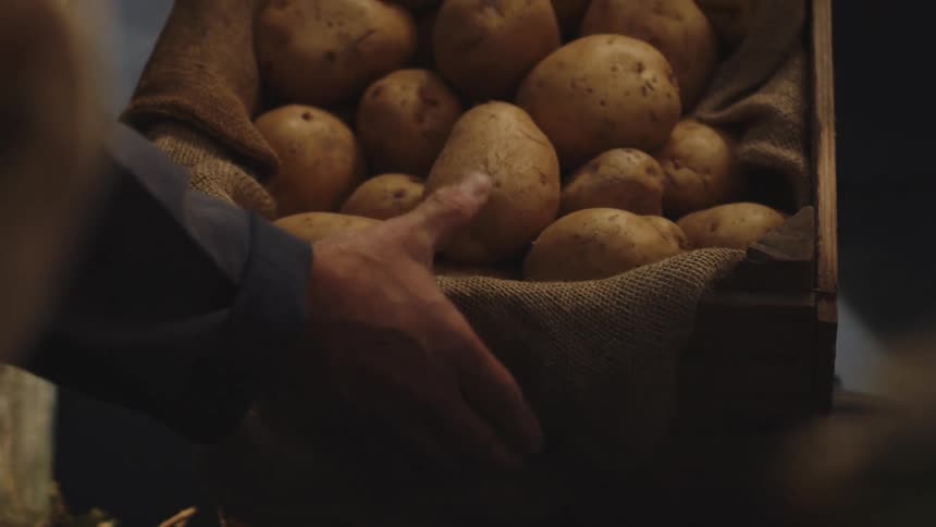 Several potatoes in a cloth inside a box that a person places on a shelf