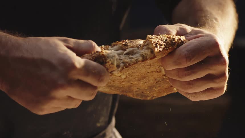Close up of a person breaking a loaf of bread with his hands