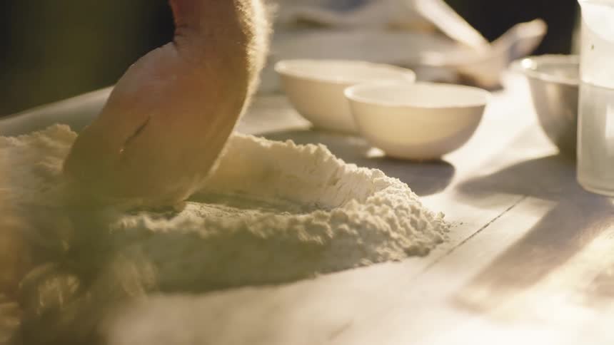 A white man moves flour around on a table