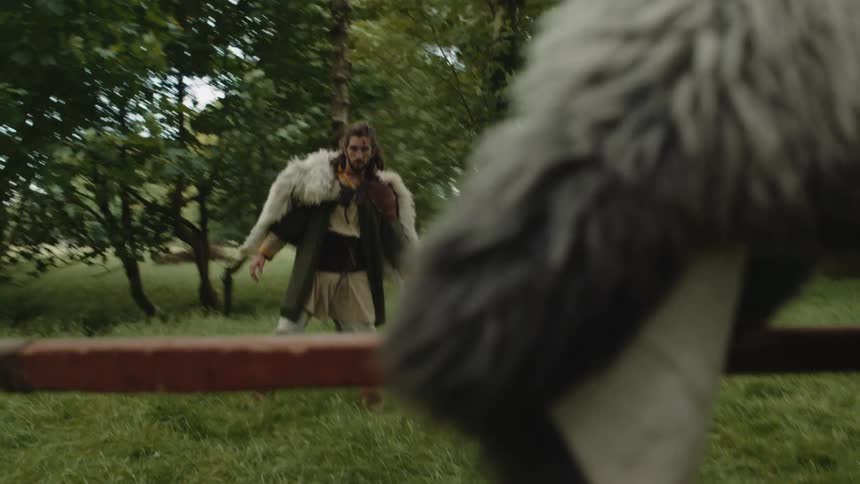 Viking holding a sword and going after another viking who is holding an ax in the middle of a forest