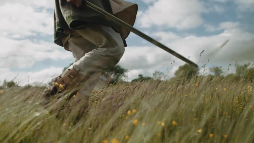 Legs of a medieval man walking in an open field with a sword