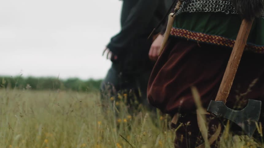 Some people walking in a reed field and one of them is using an ax and loose clothing