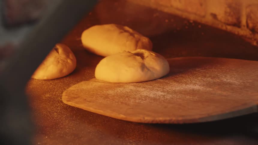 Bread dough being placed to bake in an oven