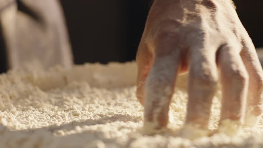 A persons hand smearing flour with a liquid on a table with sunlight