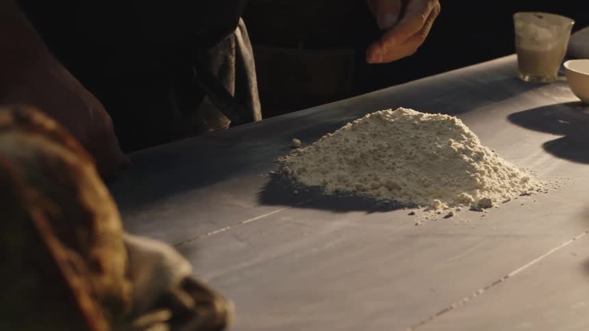 Hands pressing into a mound of flour on a table