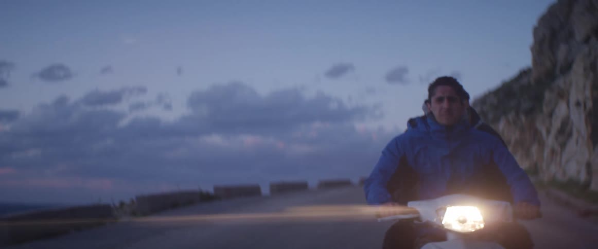 A man in a blue coat drives a motorcycle with his passenger