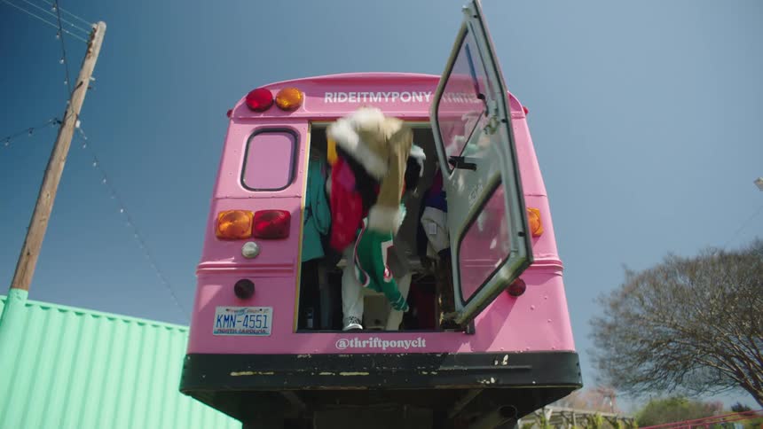 A pink bus where a person inside opens the back and throws clothes forward