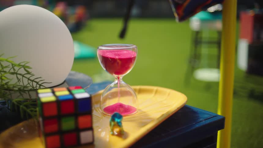 An hourglass dropping sand next to a rubiks cube outside