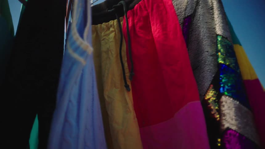 Clothes on hangers sway outside a distance from people entering a store