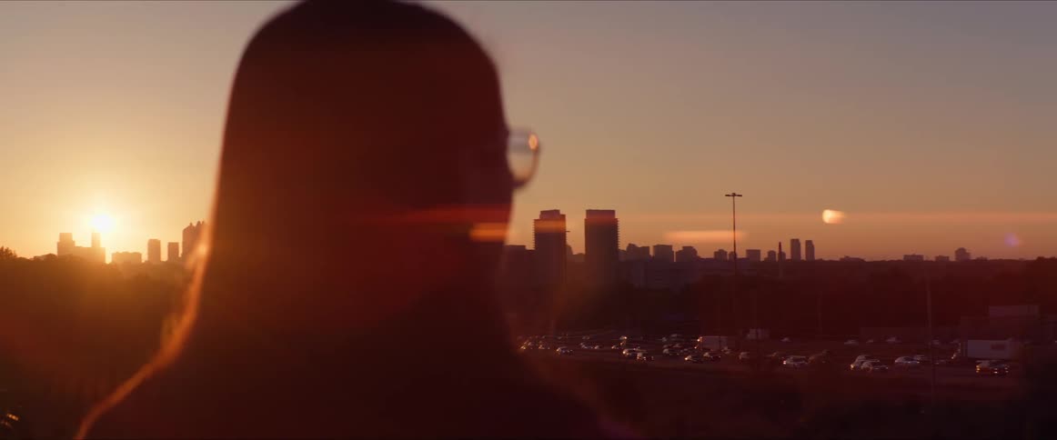 Woman stands looking at traffic flowing to and from the the city at sunset