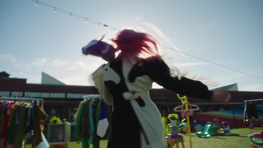 Woman selling clothes on racks on the lawn near a large store dances while wearing a sample outfit