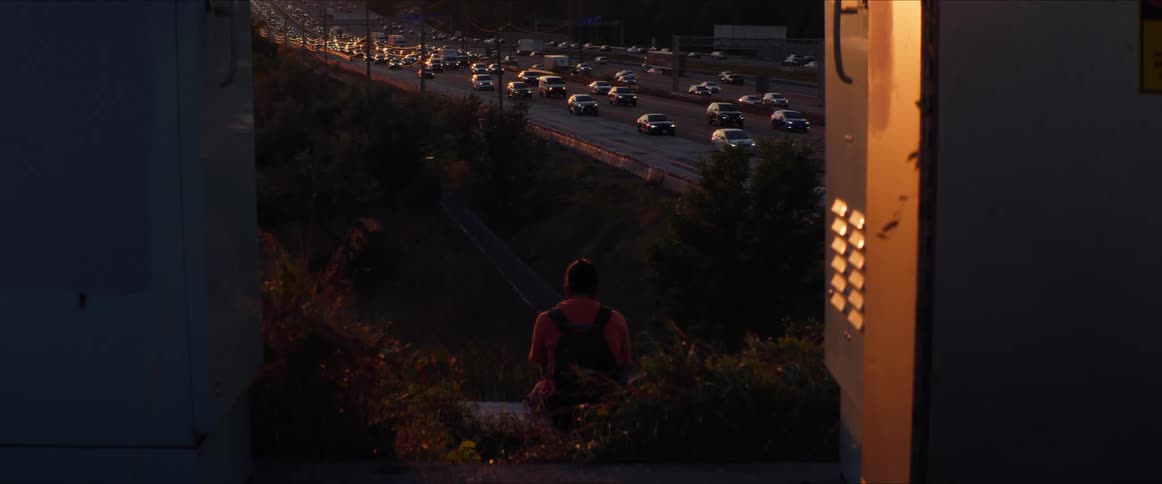 View of a person sitting with their back looking at a highway with vehicle traffic in the late afternoon