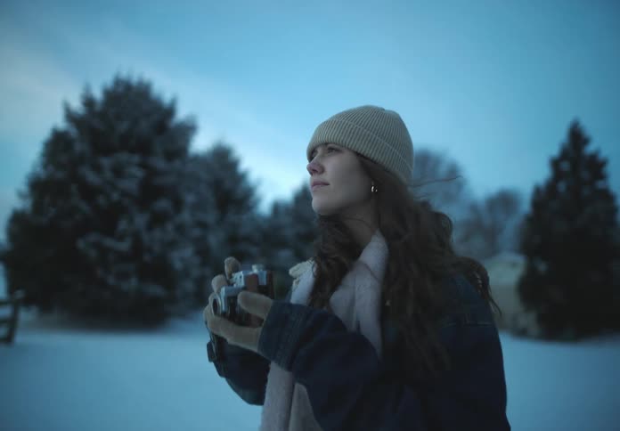 A woman in winter clothing taking a photo of a snowy landscape