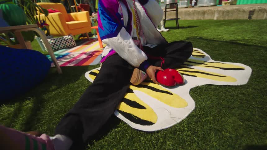 Portrait of a man sitting on the grass pretending to answer a corded phone and wearing fashionable clothes