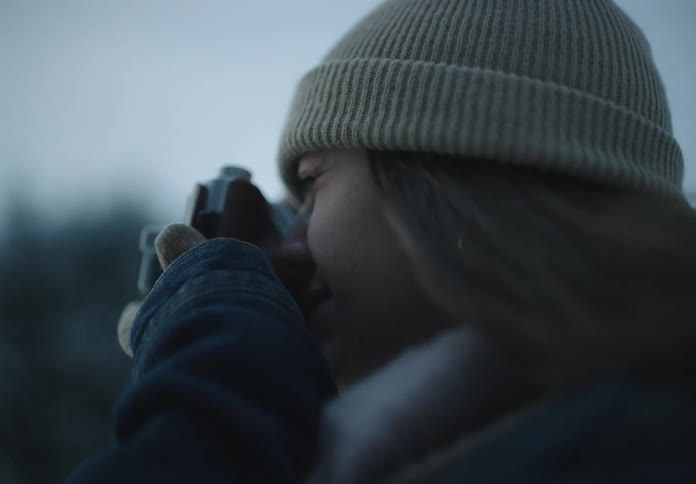 A woman in a knit beanie holds a camera up to her eye to take a photograph