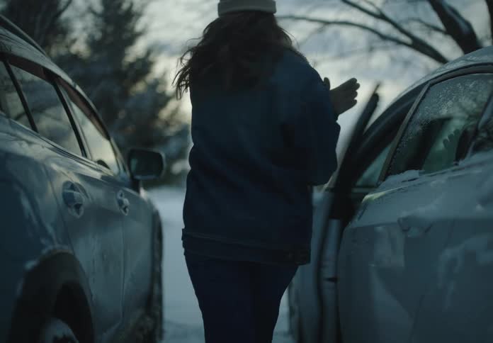 Two cars parked in a snowy clearing and a woman comes out of the drivers seat of one of them and walks off