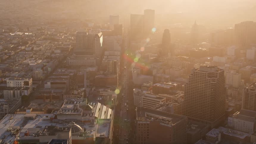 An aerial view of a city with several tall buildings and a huge street in the center and bright sunlight in the morning