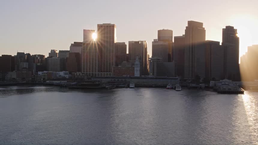 The sun shining between skyscrapers on a coastal city skyline