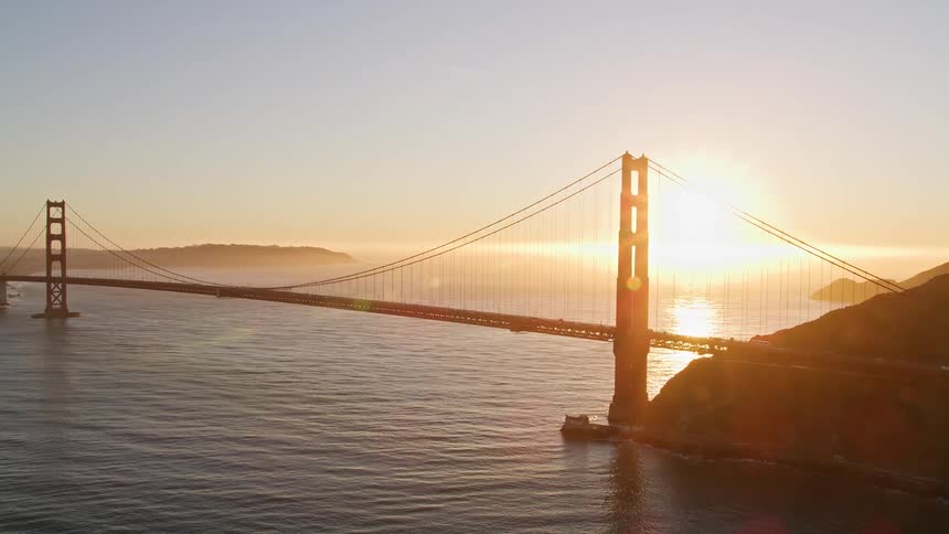 Bright sun sitting on the horizon glares through the cables of the golden gate bridge