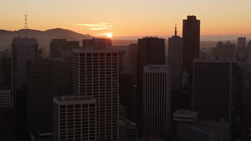 A city center with huge commercial buildings and in the background the sun rising in the morning