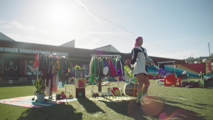 A woman dancing in front of second hand clothes racks at a fair