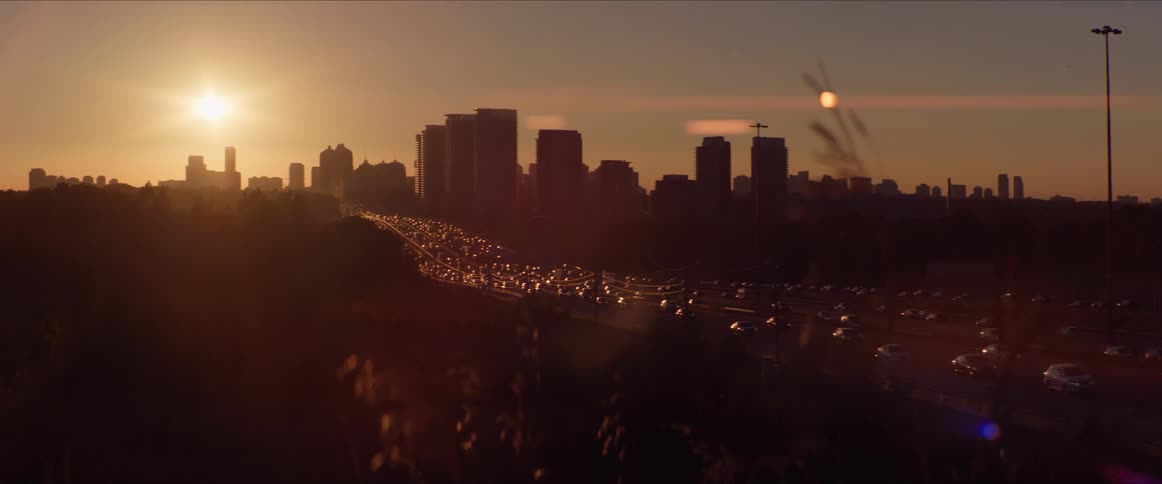 Highway with vehicle traffic and in the background a metropolis with a skyscraper and the sunset on the horizon