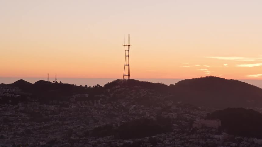 Tall structure towers over buildings nestled against hill under a red sky