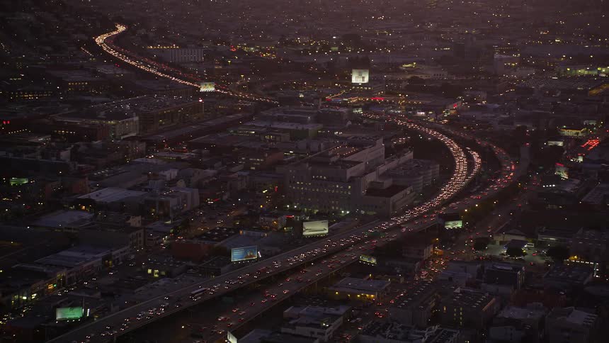 Heavy traffic flows along highways winding through city bordering mountains at night