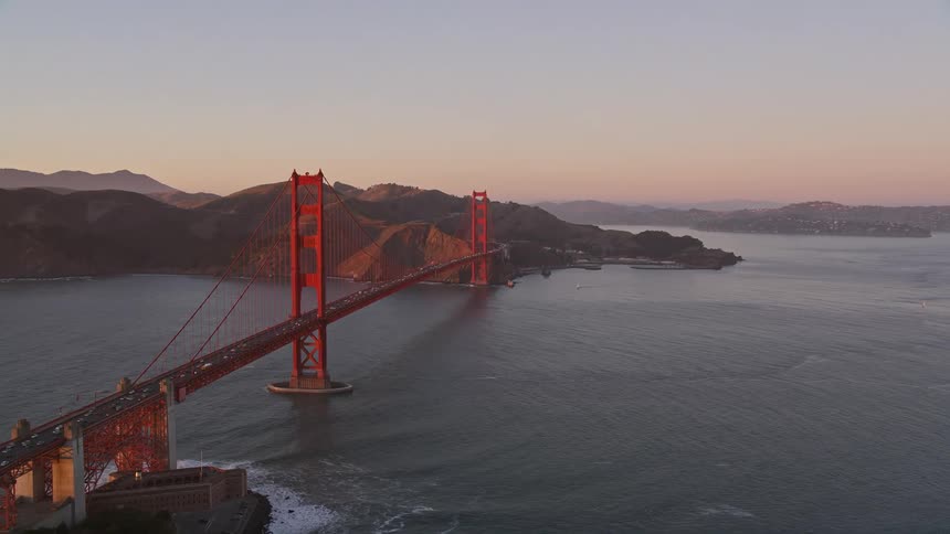 Aerial panorama of a highway leading to the golden bridge with surrounding suburbs and a reddish sky at dawn