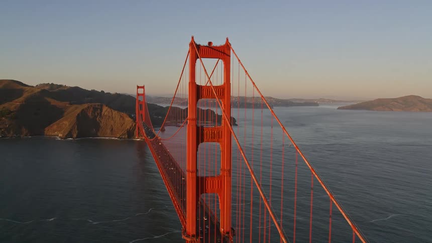 Panorama of the golden bridge over the sea and connecting mountains with vehicle traffic in a clear cloudless morning sky