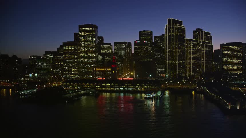A dusk in a city with huge buildings facing the sea that are reflecting the lights on the water surface