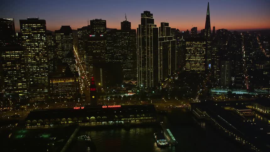 Dusk in a city with huge buildings and a very busy street with cars and the buildings have lights on