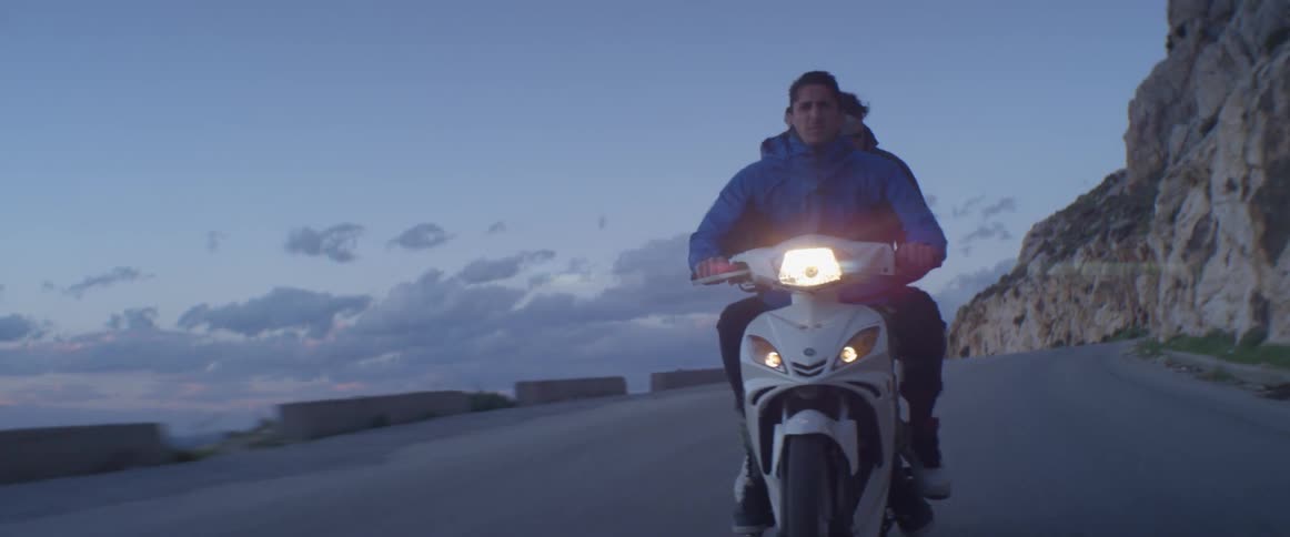 Two men riding a motorcycle down a road near water