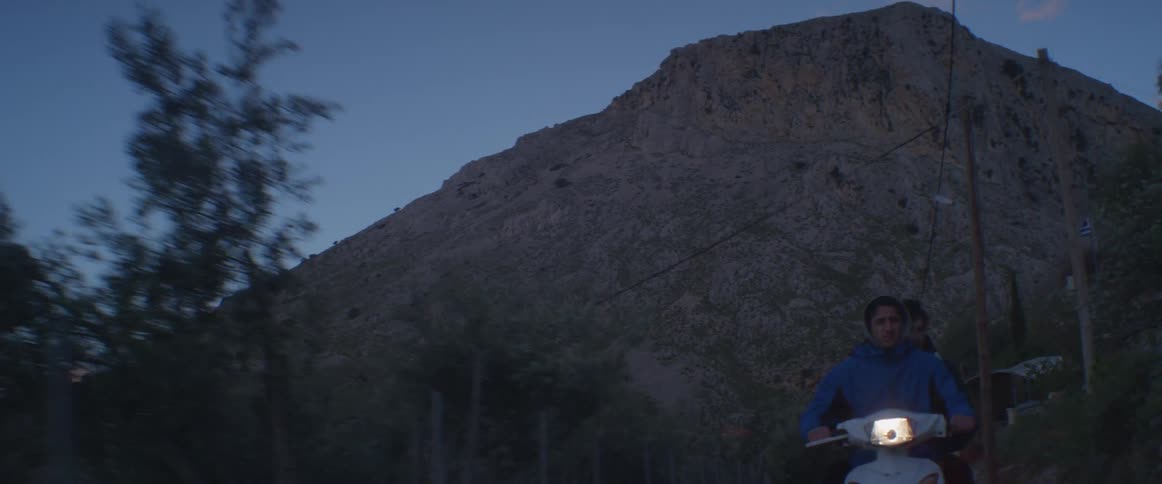 People on a motorbike riding away from a mountain at sunset