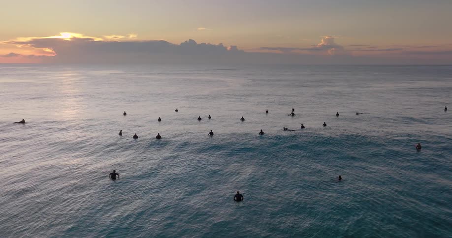 Swelling wave passes surfers floating in the ocean during sunrise