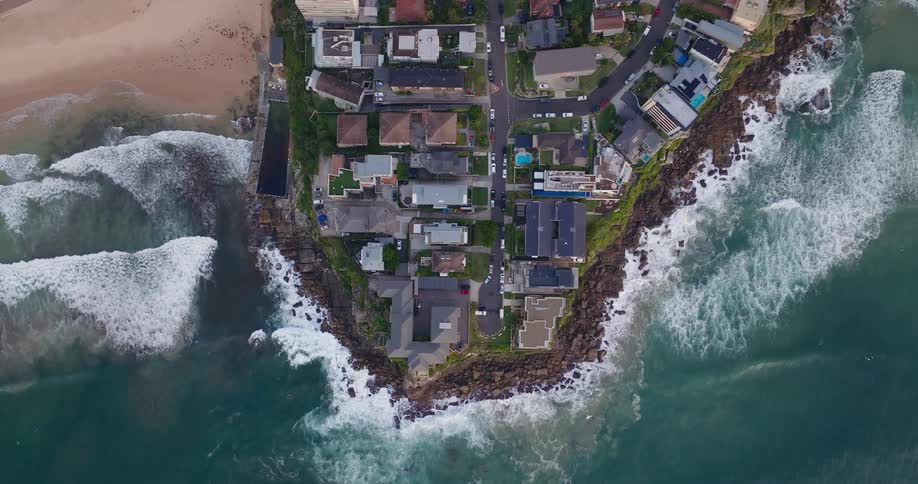 Aerial view of a cluster of luxury homes situated on a narrow strip of land between the ocean and a beach