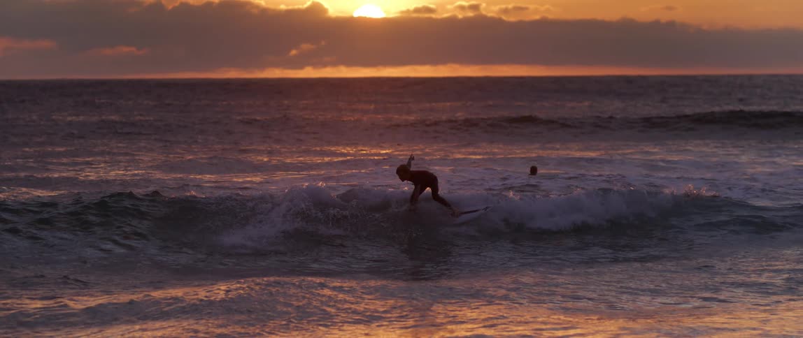 Boy surfing a small wave on the beach with sunrise on the horizon