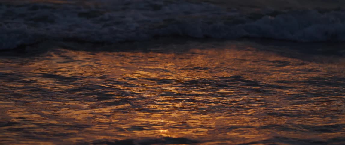 Closeup of calm waves on a beach with a reflection of early morning sunlight