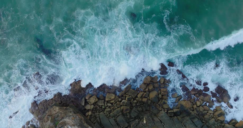 Top view of a blue sea waves crashing on the rocky shore