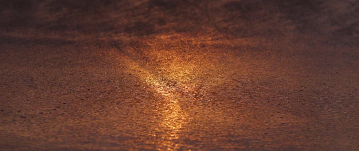 Wet beach sand with sea water and the reflection of morning sunlight