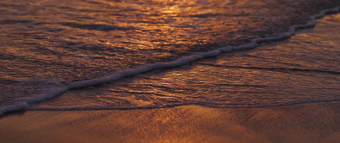 Beach sand with small sea waves and the reddish reflection of the early morning sun