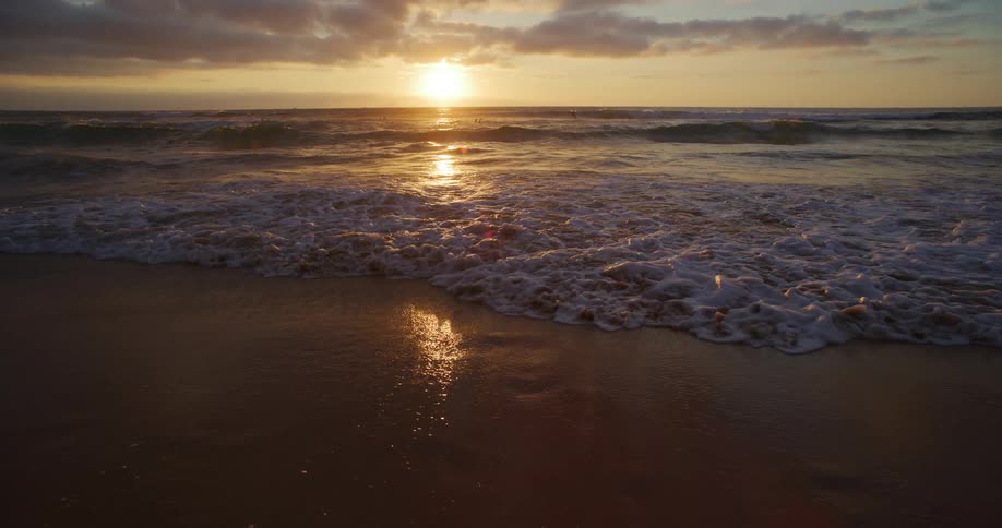 Beach landscape with calm waves on the sand and the reflection of the sunset on the horizon