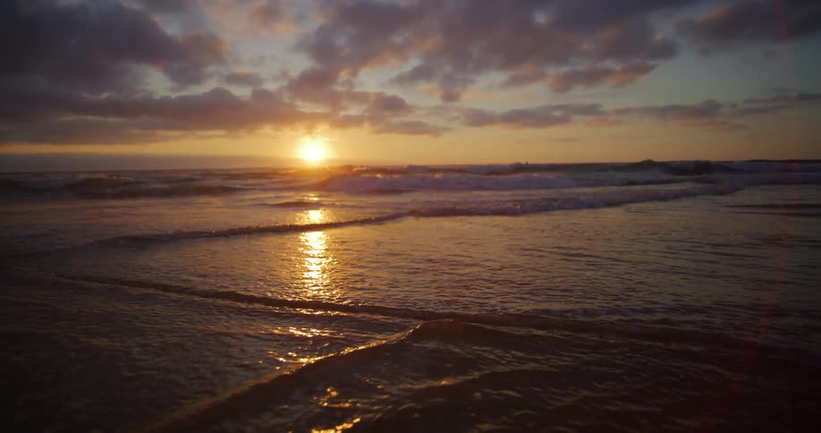 Beach landscape with calm sea waves and the sunrise in the background on the horizon