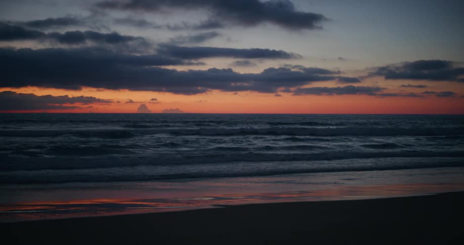 Landscape of a beach with calm waves in a reddish dawn sky