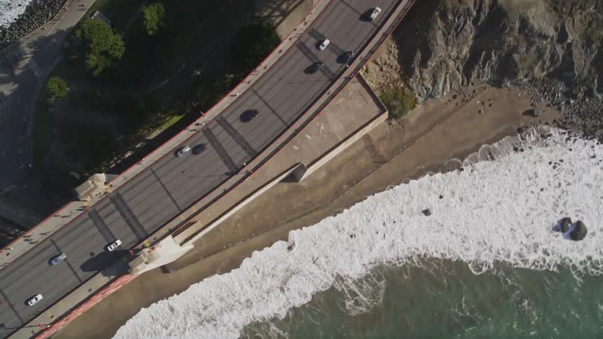 An aerial view of a coastal road with traffic next to a wavy beach