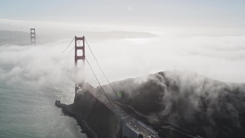 Traffic crosses golden gate bridge while dense fog covers the area